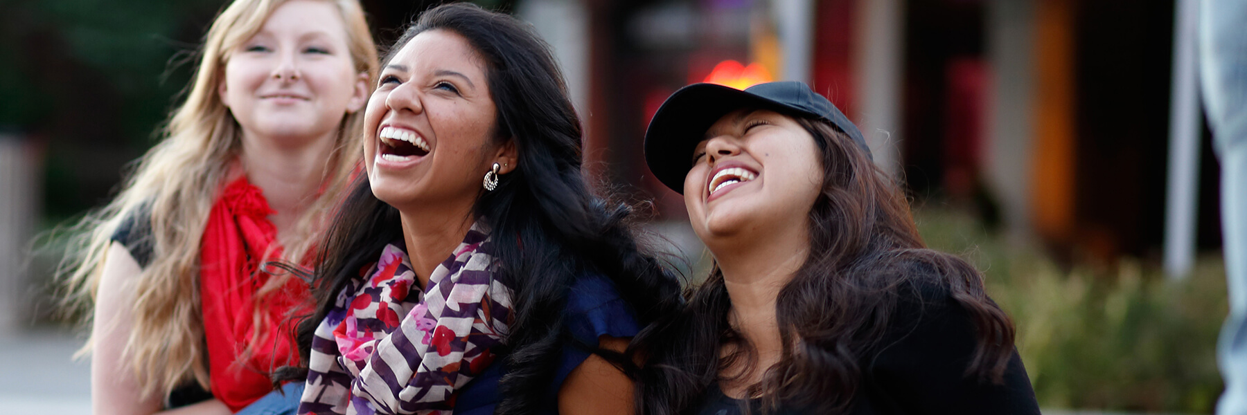 Three female students laughing together outdoors.