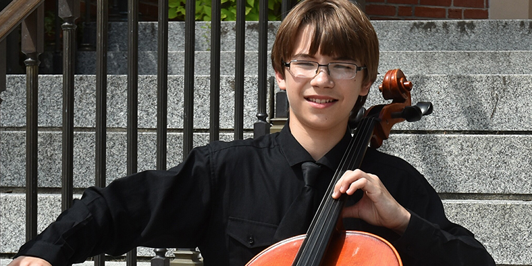 Andrew Bailey seated on stone steps posing with his cello.